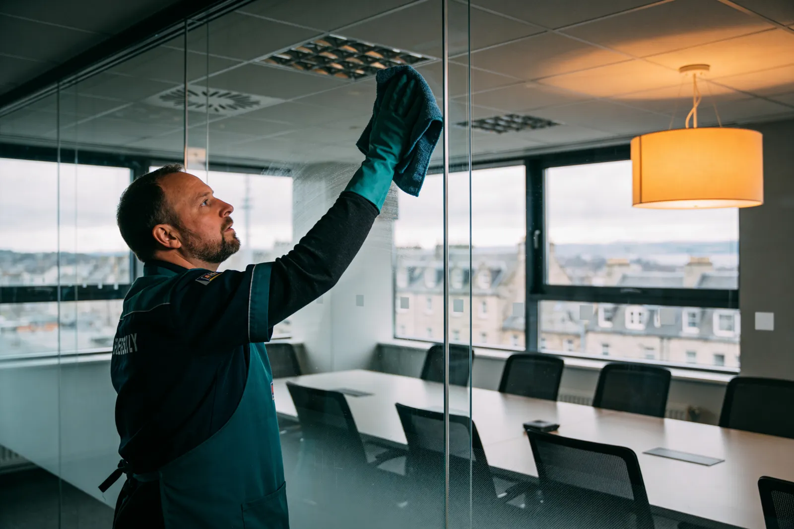 A cleaner polishing the glass wall of a modern meeting room