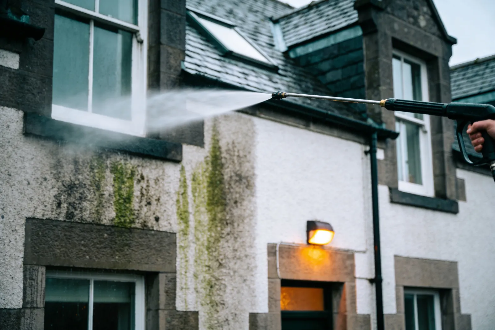 Soft washing render on a house, clean section emerging from grime